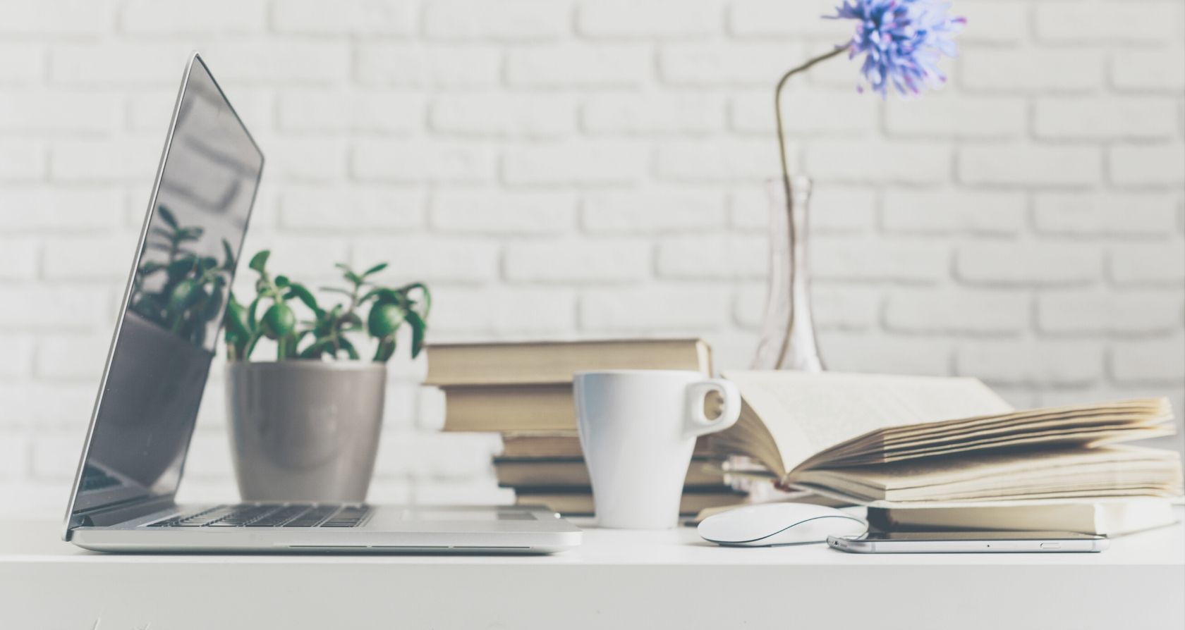 Verlassener Laptop auf dem Schreibtisch mit Büchern, Kaffee und Pflanzen. Schreibblockade!